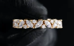 picture of a gold ring studded with stones held by a hand wearing black glove